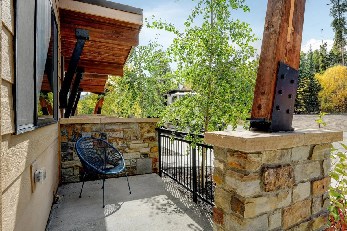 A tranquil exterior area with stone columns, wooden beams, and surrounding greenery. The seating area invites relaxation and socializing, with a peaceful mountain atmosphere that complements the excitement of local events.