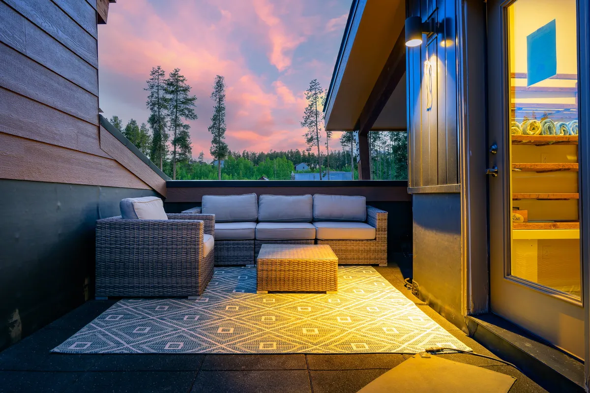 This exterior setting features a comfortable seating area on a softly lit outdoor rug, framed by a beautiful sunset sky. The space is designed for relaxing, entertaining, and enjoying panoramic views—mirroring the scene described for adults unwinding in the rooftop hot tub.