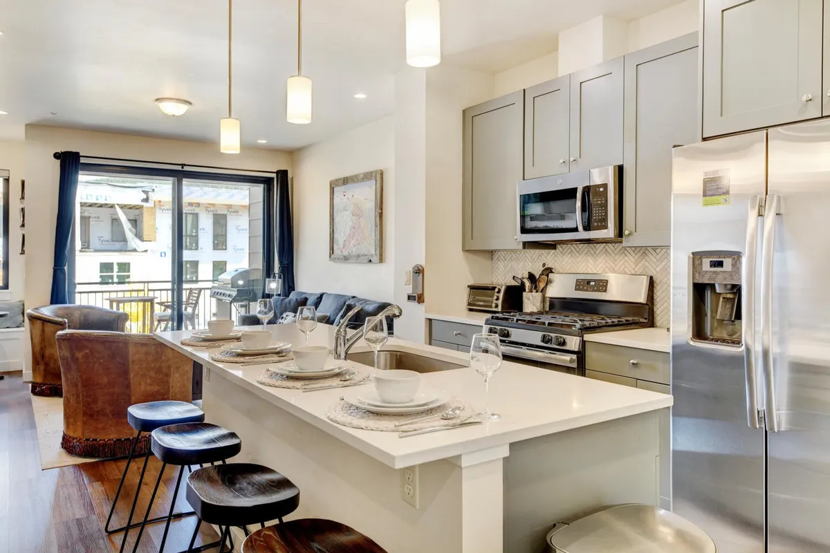 This image centers on the chef’s kitchen, featuring a large kitchen island with seating, gleaming stainless steel appliances, ample natural light from large windows, and stylish wall art. The setup invites both cooking and casual socializing, underscoring the kitchen’s role as a hub for culinary creativity and conversation.