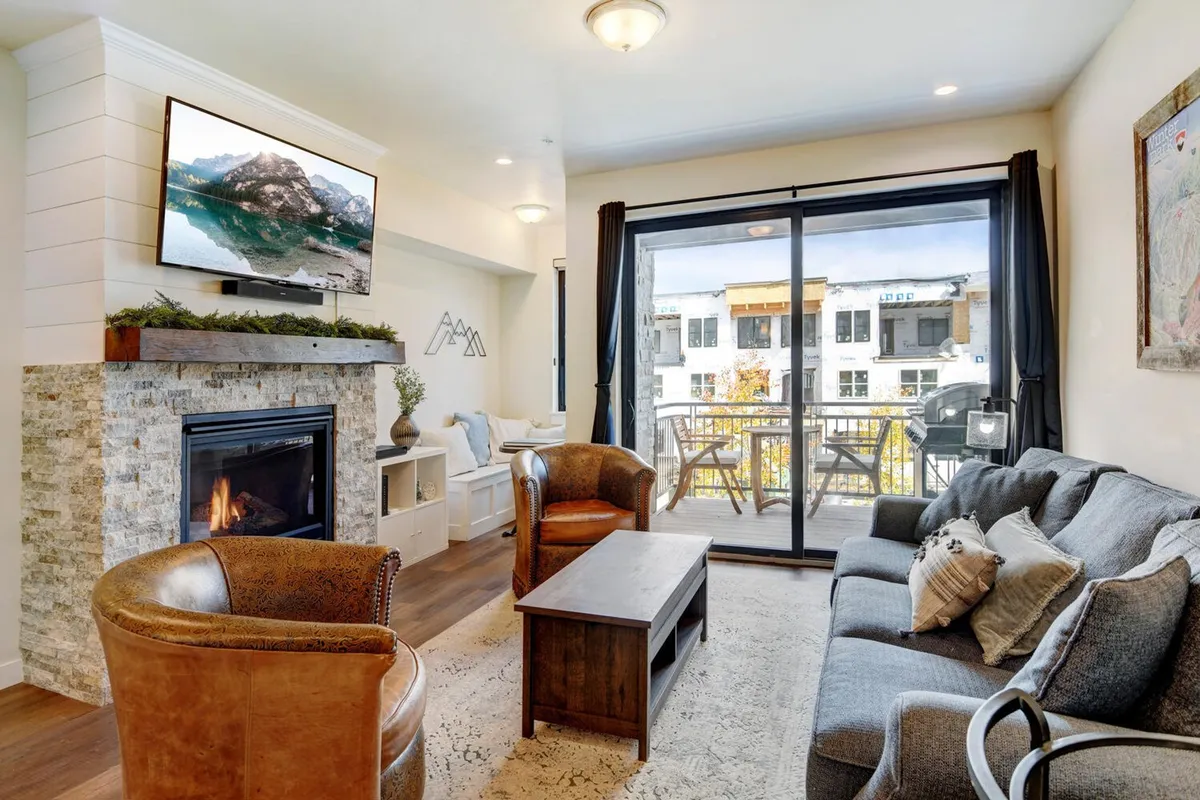 A comfortable living area with a plush sofa, stone fireplace, large television, and access to a balcony. The space is inviting for relaxing, socializing, or enjoying a movie night, with a warm ambiance enhanced by the fireplace.