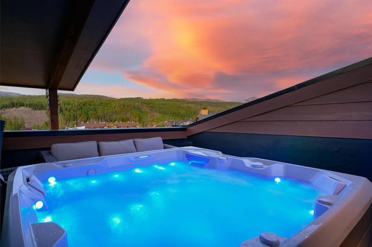 This image showcases a hot tub on a rooftop or elevated deck, framed by sweeping mountain views and a dramatic, colorful sunset sky. The inviting water, scenic backdrop, and tranquil mood perfectly evoke relaxation and high-altitude serenity.