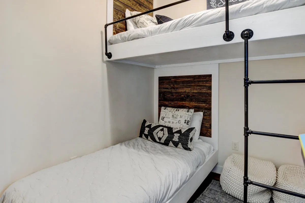 A cozy bunk room with a rustic wooden accent wall, neatly made bunk beds with decorative pillows, and a soft, textured rug. The space is inviting and ideal for families or groups seeking comfort and a sense of home.