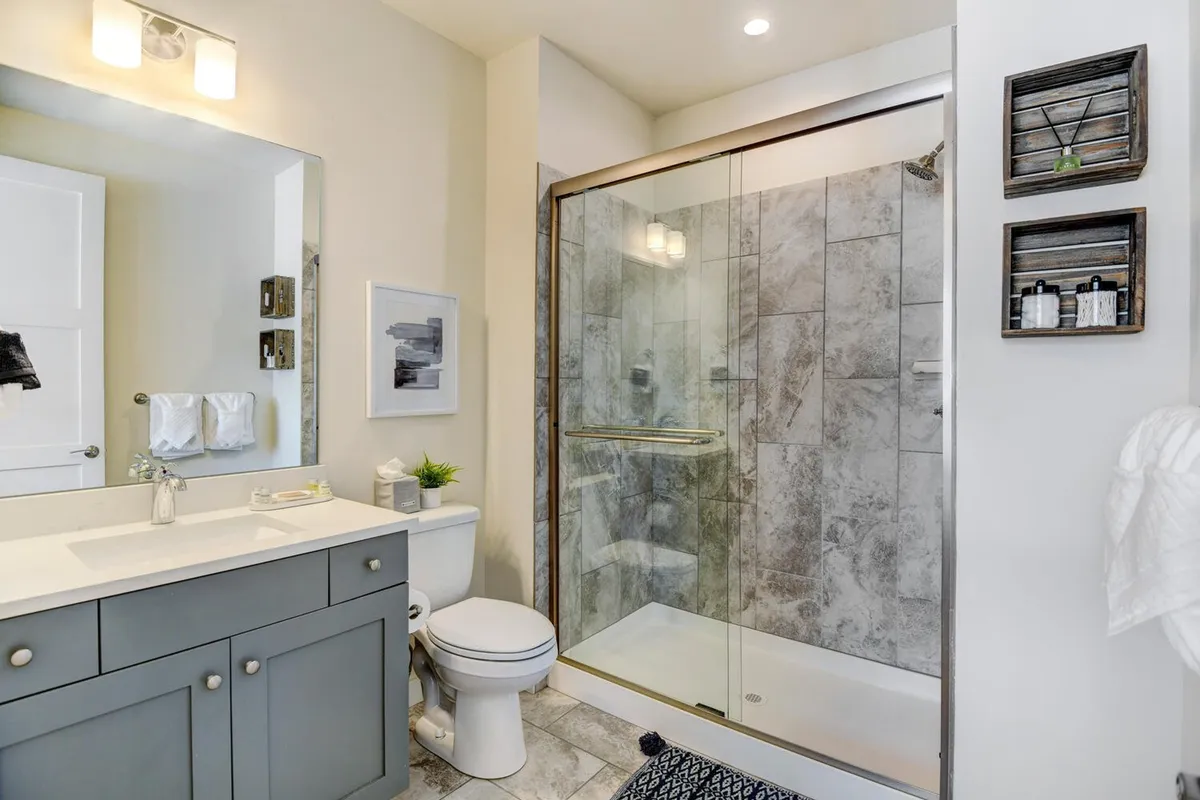 A modern bathroom featuring a glass-enclosed shower, a vanity with elegant sink, decorative shelving with spa-quality toiletries, and framed artwork. The space is bright, fresh, and evokes a spa-like ambiance.
