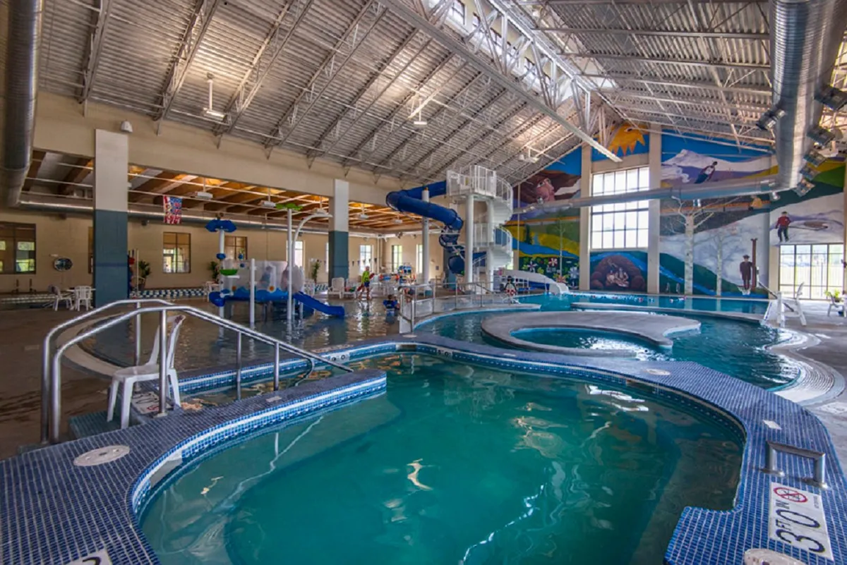 An energetic interior scene at a recreation center featuring colorful water slides, pools, and a vibrant mural, with families and kids enjoying swimming and playful water activities.
