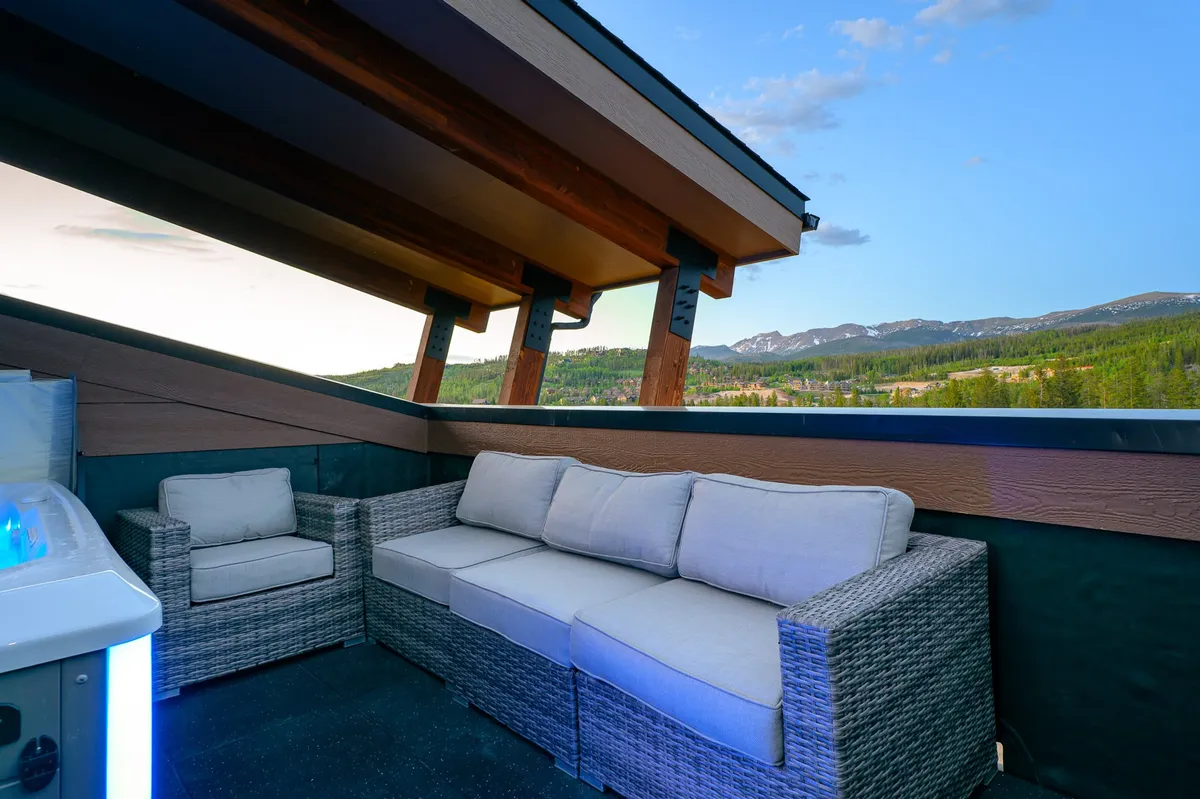 A tranquil exterior setting with a spacious seating area, a mountain backdrop, and a hot tub perfect for sunrise or starlit relaxation. The space evokes the spirit of outdoor adventure and connection to nature, with inviting features for both leisure and socializing.
