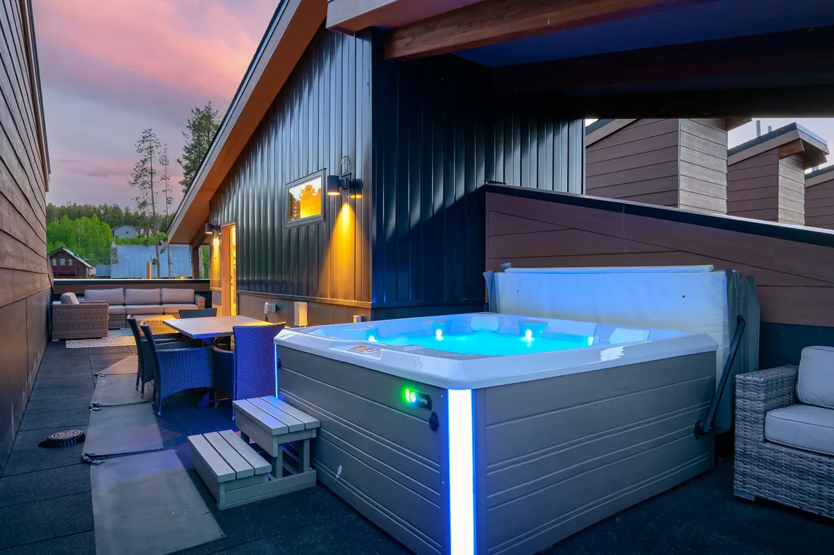 This image focuses on an inviting hot tub paired with a spacious outdoor seating and dining area, set against a glowing sunset. The scene exudes warmth, comfort, and possibilities for both intimate and group experiences.
