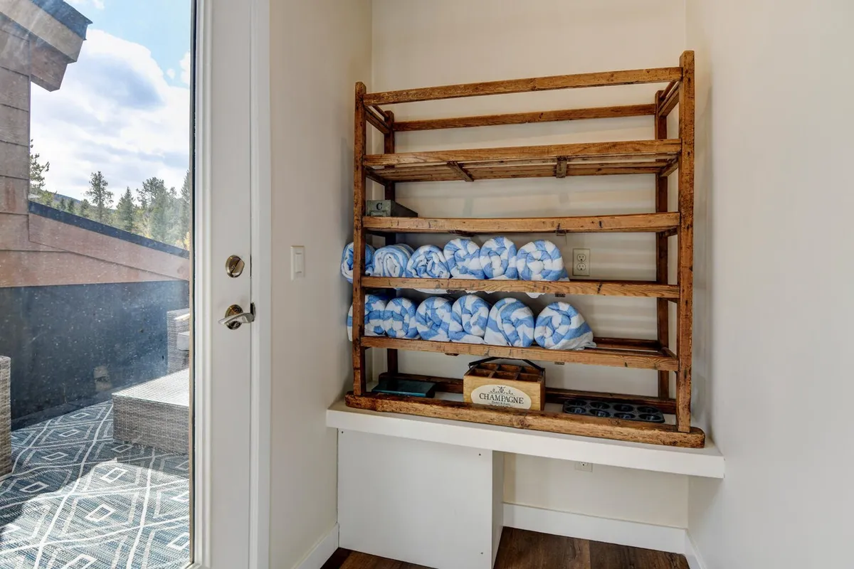 A set of wooden shelves neatly arranged with plush, rolled towels and spa accessories, creating a subtle but distinct spa-like vibe within the home.