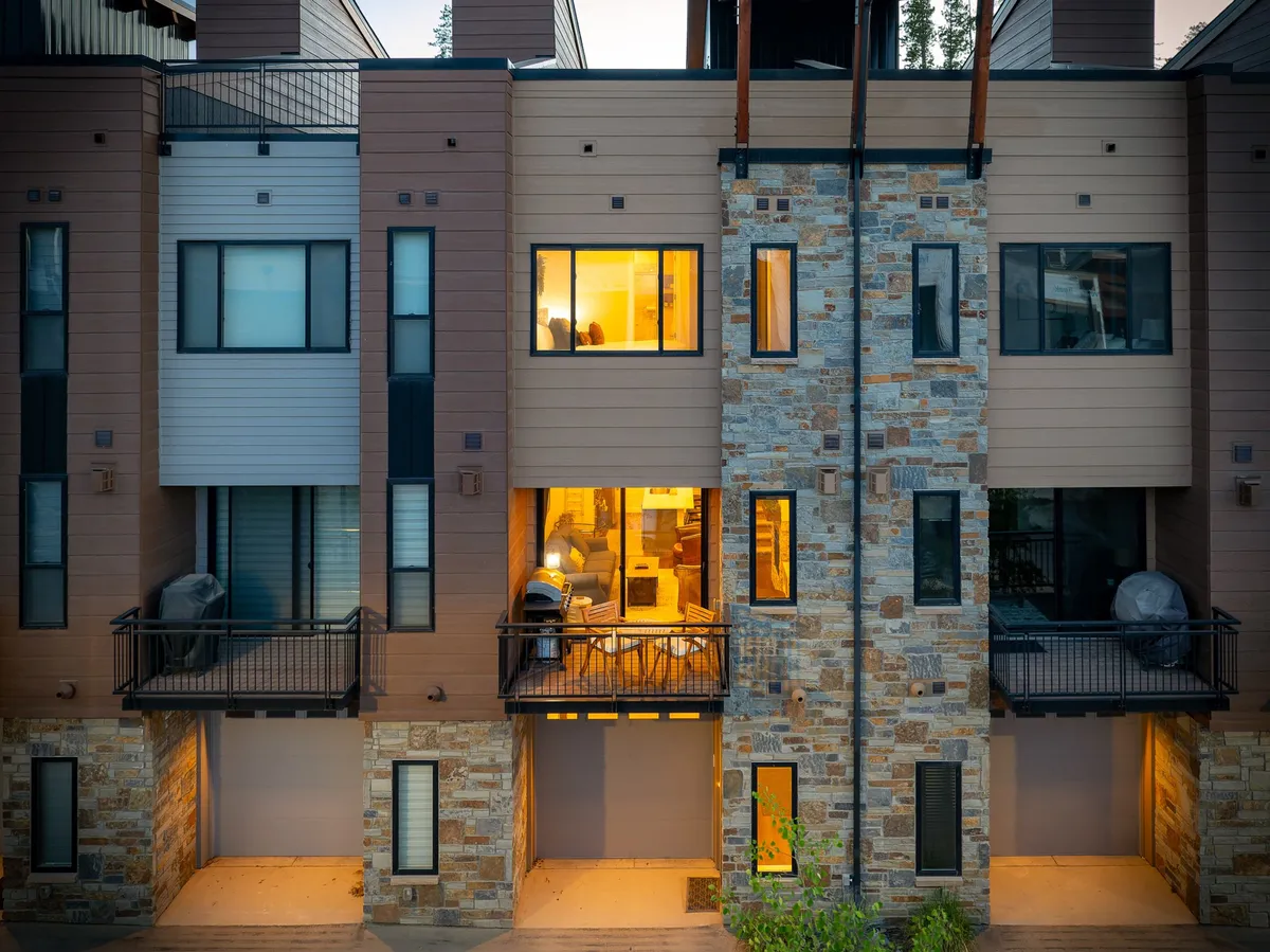 This exterior image showcases the townhome's stone facade, large windows glowing with warm light, and inviting balconies. The welcoming atmosphere is enhanced by the sense of indoor-outdoor connection, hinting at comfortable evenings and family gatherings inside.