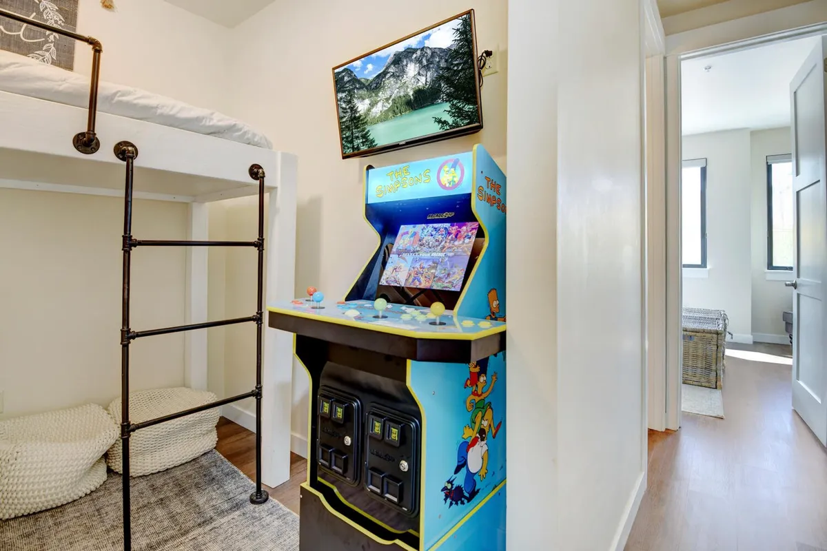 A cozy bunk room is shown with a sturdy bunk bed, an arcade game, and a wall-mounted TV. The room’s design encourages both gaming and movie nights in a playful, comfortable setting.