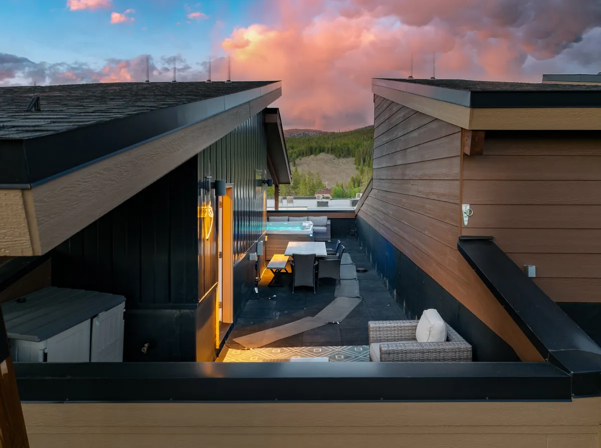 A rooftop patio with a dining table and broad views of the surrounding landscape, suggesting space for both relaxation and entertainment. The scene is open, airy, and ready for memorable moments with loved ones.