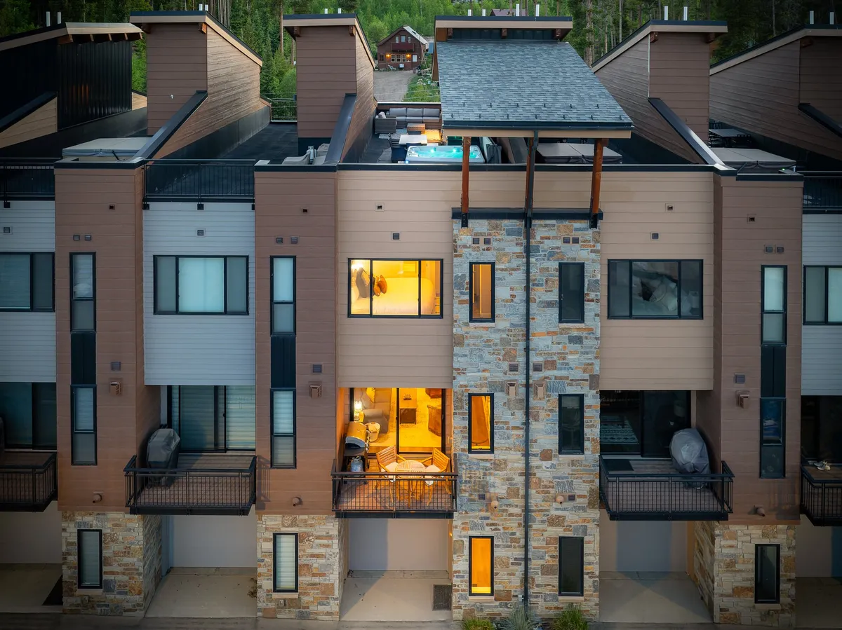 A welcoming exterior view of the luxury townhome, featuring illuminated windows, stone facade, and inviting balconies. The mood is cozy yet sophisticated, suggesting both privacy and comfort—an ideal home base for returning from daily adventures.